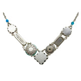 The La Dolce Vita V Multi-Color Necklace by Firefly is a handmade silver piece with a V-shaped decorative metal, engraved with a floral design and dream, featuring small blue beads, crafted through fair-trade practices.
