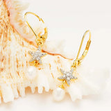 The Gold Vermeil Starfish Pearl Drop Earrings by Shanore feature starfish designs with small crystals and dangling pearls, elegantly displayed against a textured seashell backdrop.