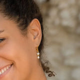 Close-up of a smiling person showcasing Shanores Gold Vermeil Starfish Pearl Drop Earrings. The image focuses on the left ear, featuring the stunning ocean-themed design, with part of their cheek and a glimpse of their mouth visible against a softly blurred background.