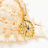 The Shanore Gold Vermeil Blue Sapphire Compass Necklace showcases a gold compass rose pendant with black and white stones, a central lab-grown sapphire, and cardinal direction details. Its elegant necklace design beautifully complements ocean themes.