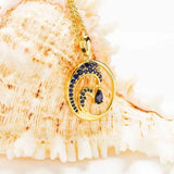 The Shanore Gold Vermeil Blue Sapphire Wave Necklace epitomizes beach jewelry, showcasing a wave-shaped pendant with blue lab-grown sapphires against a textured seashell background.