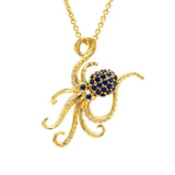 The Shanore Gold Vermeil Blue Sapphire Octopus Necklace showcases an enchanting octopus pendant adorned with blue lab-grown sapphires on its head. Clear gemstones adorn the tentacles, elegantly hanging from a fine gold chain.