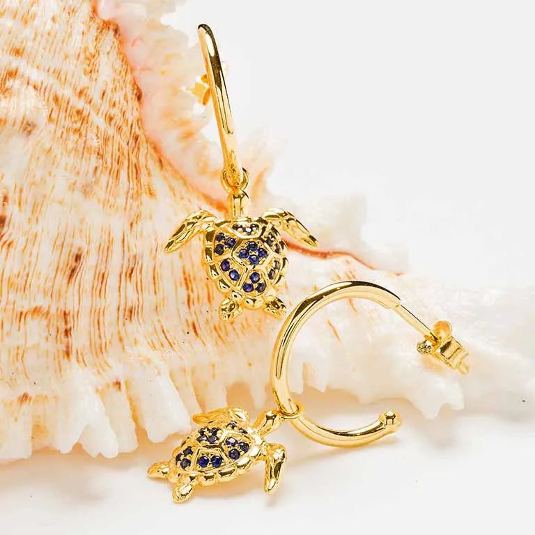Shanores Gold Vermeil Blue and White Sapphire Turtle Earrings- Ocean Jewelry is showcased against a seashell. The turtle design with detailed craftsmanship and vibrant sapphires beautifully captures the marine theme.