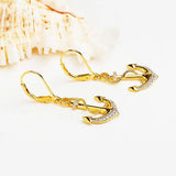 Shanores Gold Vermeil Anchor Drop Earrings from the Ocean Jewelry collection, adorned with cubic zirconia crystals, rest elegantly on a white surface with a seashell backdrop.