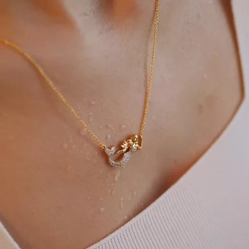 Close-up of a person wearing Shanores Gold Vermeil Mermaid Necklace - Ocean Jewelry. The pendant shimmers with small stones, capturing light beautifully, while a blurred background highlights the necklaces elegance against the skin.