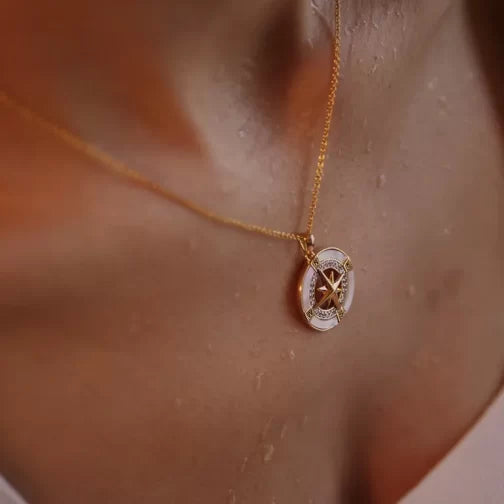 Close-up of a person wearing the Shanore Gold Vermeil Mother of Pearl Compass Necklace, featuring an intricate star pattern. It rests against dewy skin with a softly blurred background.