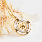 The Shanore Gold Vermeil Mother of Pearl Compass Necklace features a rose pendant encircled by small diamonds, elegantly set on a seashell. It hangs from a delicate gold chain, beautifully showcased against a light backdrop.