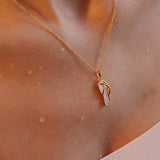 Shanores Gold Vermeil Mother of Pearl Flip Flop Necklace lies elegantly on skin and neck, set against a textured peach garment. Water droplets amplify the necklace’s shimmering effect in the background.