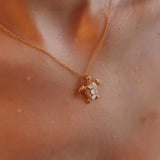 A close-up of the Gold Vermeil Mother of Pearl Turtle Necklace by Shanore reveals its exquisite turtle pendant in gold and white. Against wet skin, it suggests a recent swim, with glistening water droplets enhancing the allure of this ocean jewelry piece.