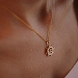 Close-up of a person wearing Shanores Gold Vermeil Mother of Pearl Ship Wheel Necklace, showcasing the beautiful Ocean Jewelry. The slightly wet skin creates a glossy effect, highlighting the exquisite piece against the smooth background.