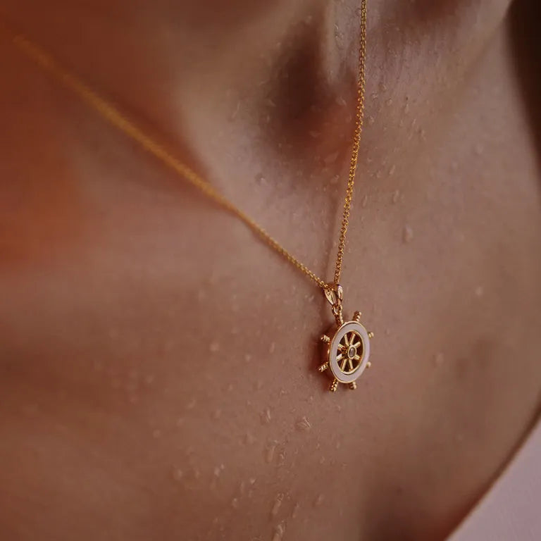 Close-up of a person wearing Shanores Gold Vermeil Mother of Pearl Ship Wheel Necklace, showcasing the beautiful Ocean Jewelry. The slightly wet skin creates a glossy effect, highlighting the exquisite piece against the smooth background.