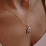 The Gold Vermeil Sand Dollar Necklace by Shanore graces the neck with an ornate pendant, resembling a delicate sand dollar, and complements the slightly glistening skin against a light top.