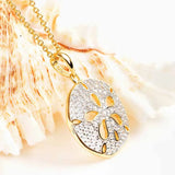 The Shanore Gold Vermeil Sand Dollar Necklace, adorned with cubic zirconia, is beautifully showcased against a seashell backdrop, highlighting its intricate detailing for an elegant beach-inspired look.