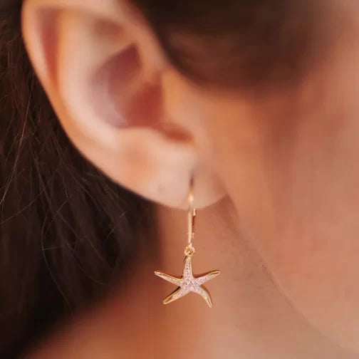 Close-up of an ear wearing Shanores Gold Vermeil Starfish Earrings from the Ocean Jewelry collection, featuring shimmering detail and textured vermeil surface. The earrings dangle gently against warm skin, accented by cubic zirconia and a softly blurred background that enhances their elegance.