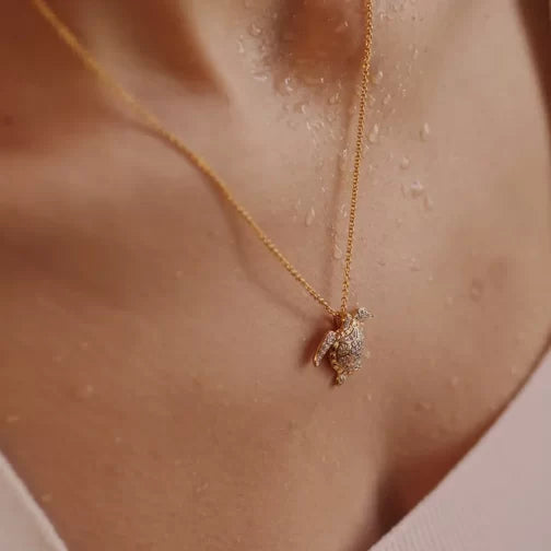 A close-up captures a person wearing the Shanore Gold Vermeil Turtle Necklace- Ocean Jewelry, its cubic zirconia pendant sparkling. Water droplets on their skin create a fresh look, while the softly blurred background highlights the necklace’s intricate 14k gold details.