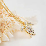 The Shanore Gold Vermeil Turtle Necklace, from the Ocean Jewelry collection, features a turtle-shaped pendant crafted in 14k gold with sparkling cubic zirconia on a gold chain, set against a textured seashell backdrop.