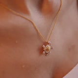 A close-up shows a woman wearing the Gold Vermeil Shell Turtle Necklace by Shanore, featuring a delicate pendant encrusted with sparkling cubic zirconia. It hangs elegantly against her skin while a softly blurred background enhances its charm.