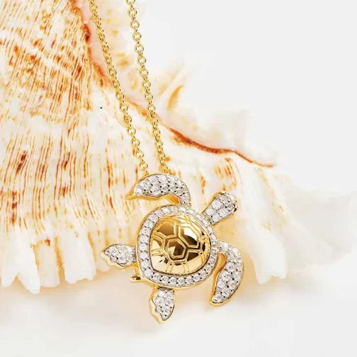 The Gold Vermeil Shell Turtle Necklace by Shanore features a gold turtle pendant with cubic zirconia accents on a delicate chain, set against an off-white seashell background.