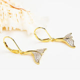 Shanores Gold Vermeil Whale Tail Drop Earrings glimmer beside a large white seashell on a light surface, reminiscent of Cubic Zirconia Earrings.