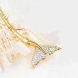 This stunning Shanore Gold Vermeil Whale Tail Necklace, set against a light background with a white seashell, features a dazzling cubic zirconia-encrusted pendant that captures oceanic elegance.