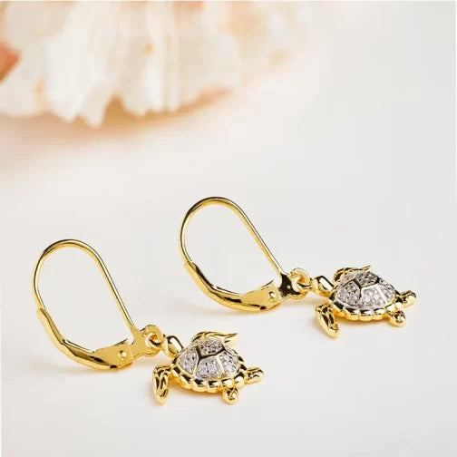 The Gold Vermeil Turtle Drop Earrings from Shanores Ocean Jewelry collection are elegantly displayed against a soft, blurred backdrop, featuring lever-back clasps with silver accents and sparkling cubic zirconia, exuding sophisticated playfulness.