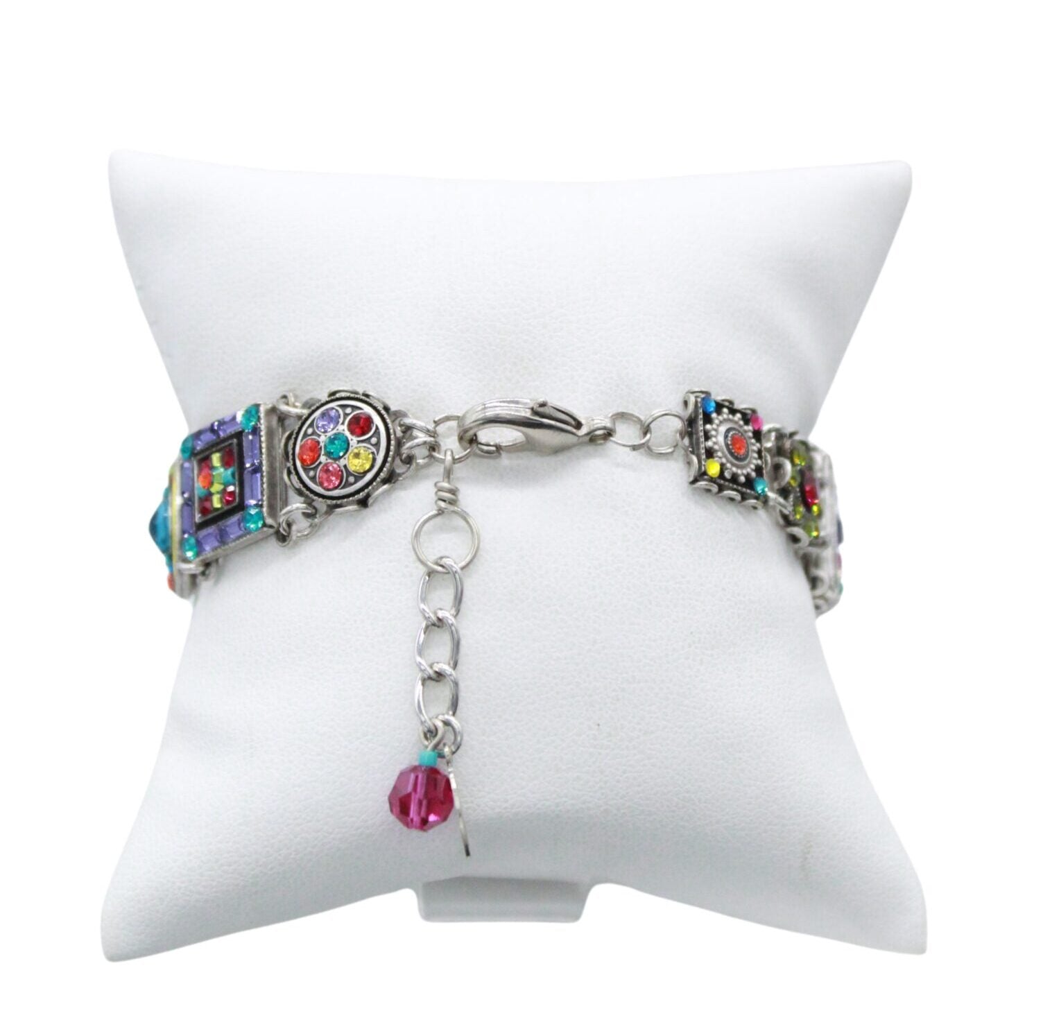 Presenting the Firefly La Dolce Vita Multi-Color Bracelet, a handmade jewel with intricate patterns and multicolored accents on a white cushion backdrop. It includes square and round elements, a chain clasp, and features a dangling red bead charm. Crafted using fair-trade practices.