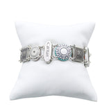 The Firefly La Dolce Vita Multi-Color Bracelet boasts a stunning silver tone and fair-trade craftsmanship. Its floral-patterned links and oval plate engraved with dream are beautifully displayed on a white cushioned stand.