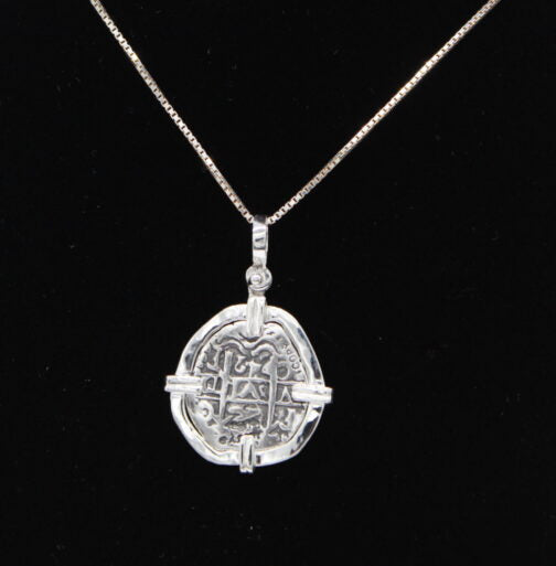 The Treasure Shoppe Inc.s Atocha 302 Coin Pendant resembles a mysterious Sterling silver Atocha coin with symbolic inscriptions set in a cross-shaped frame. Hanging elegantly against a black background, it whispers tales of historical significance.