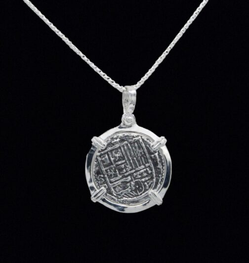 This exquisite Bogota Coin pendant by The Treasure Shoppe Inc. is crafted in sterling silver with intricate engravings, framed in a simple bezel, set against a black background, and makes for an elegant addition to any chain.