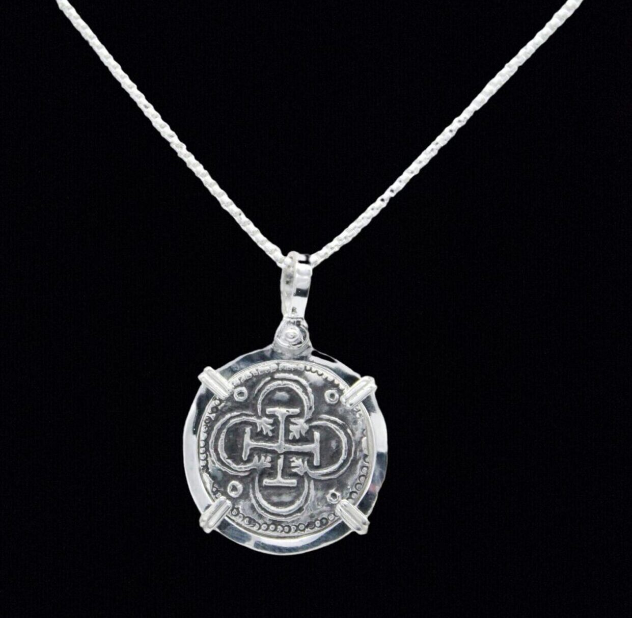 The Treasure Shoppe Inc. offers the Bogota Coin- Atocha Shipwreck Coins pendant, resembling an ancient coin with an ornate cross design encircled by intricate patterns. Its set in a sterling silver bezel but does not include a chain.