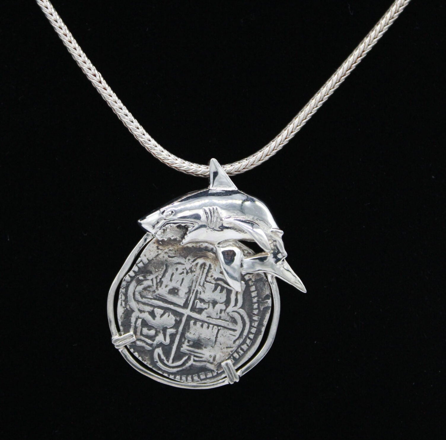 Explore The Treasure Shoppe Inc.’s 8 Reale Shark Coin: a stunning silver pendant featuring a shark design around an ancient coin, set in sterling silver. The engraved coin hangs elegantly, offering timeless elegance.
