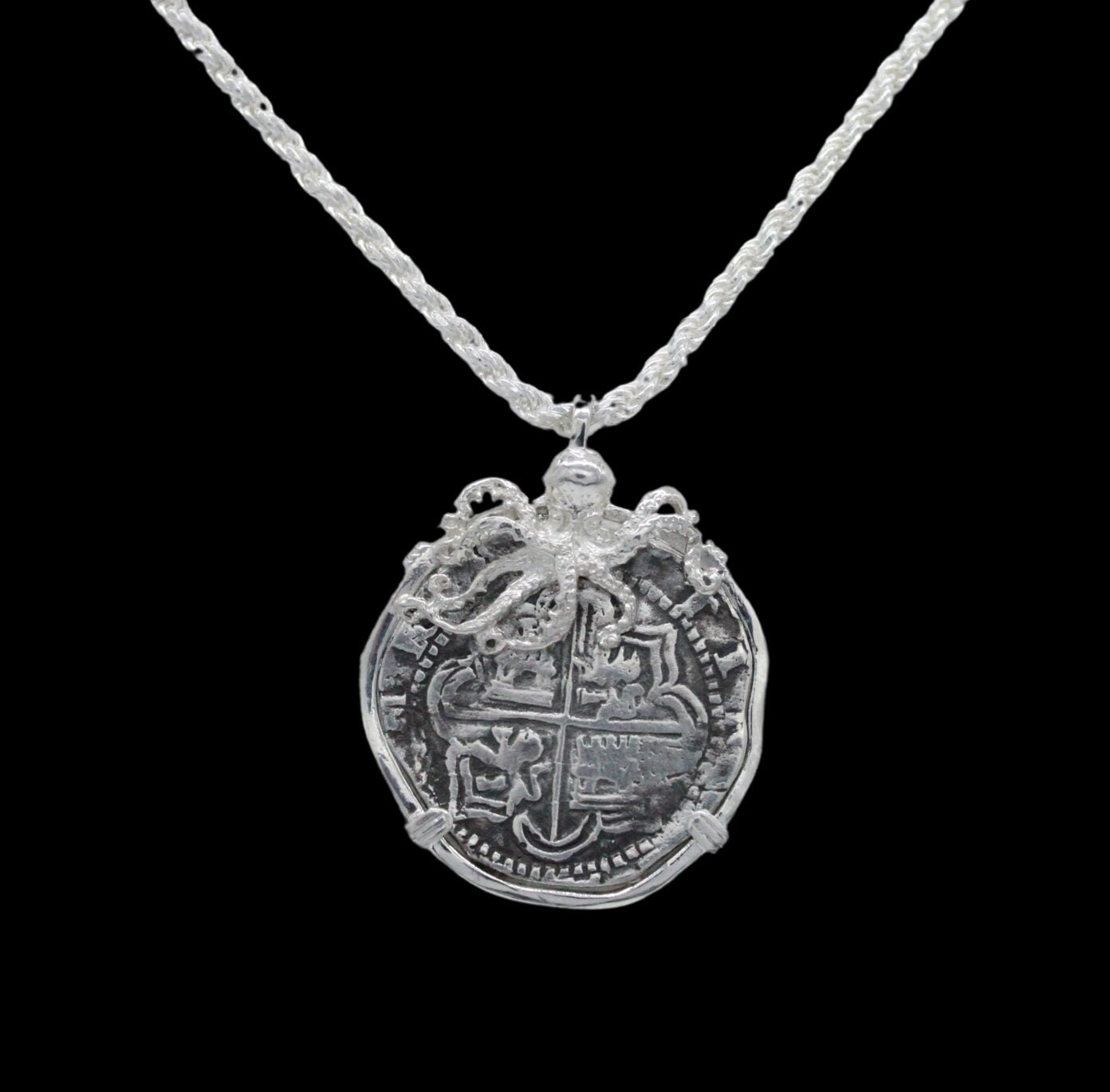 The Treasure Shoppe Inc.s Large Octopus Coin - Atocha Shipwreck pendant features an intricately designed medallion styled like an old coin, topped with a small octopus figure and encased in a sterling silver bezel, hanging from a braided silver chain against a black background.