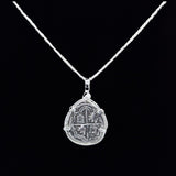 The Treasure Shoppe Inc.s Reale/Oblong Silver Frame Coin pendant features a rustic, coin-like design inspired by historic Nuestra Señora de Atocha coins. Its intricate patterns create an antique feel against a black backdrop, making it stand out on any fine silver chain.