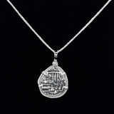 The Treasure Shoppe Inc. offers the Reale/Oblong Silver Frame Coin-Atocha Shipwreck Coins pendant, featuring a unique irregular pendant resembling an ancient coin with intricate engravings in a minimalist silver frame and black backdrop.