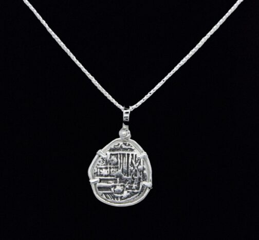 The Treasure Shoppe Inc. offers the Reale/Oblong Silver Frame Coin-Atocha Shipwreck Coins pendant, featuring a unique irregular pendant resembling an ancient coin with intricate engravings in a minimalist silver frame and black backdrop.