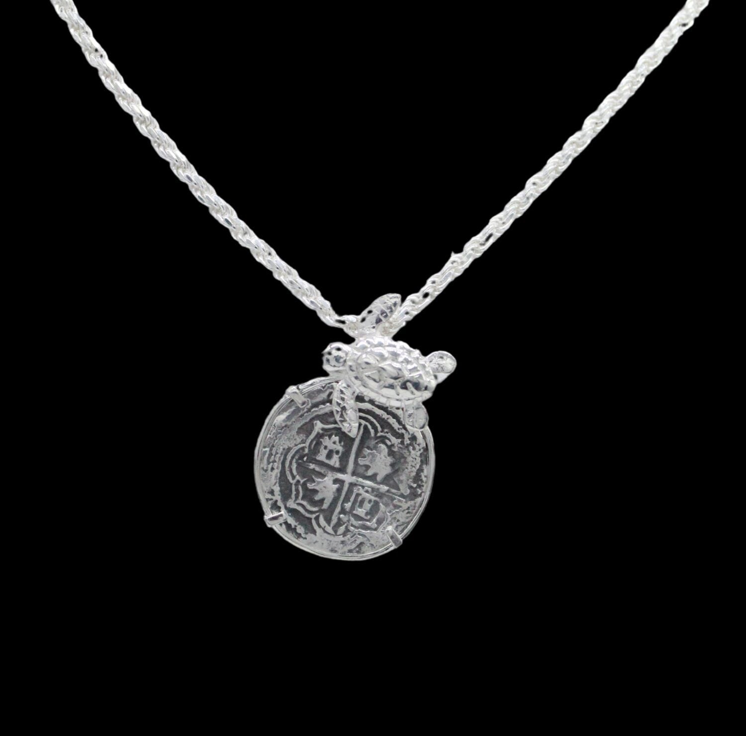 The Treasure Shoppe Inc. offers the Silver Medium Turtle Coin pendant, reminiscent of Atocha shipwreck coins, featuring a cross design and encased in a sterling silver bezel. Note: This is the pendant only; chain not included.