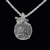 A Silver Medium Turtle Coin pendant from Atocha Shipwreck Coins by The Treasure Shoppe Inc. hangs intricately against a twisted rope chain on a black background.