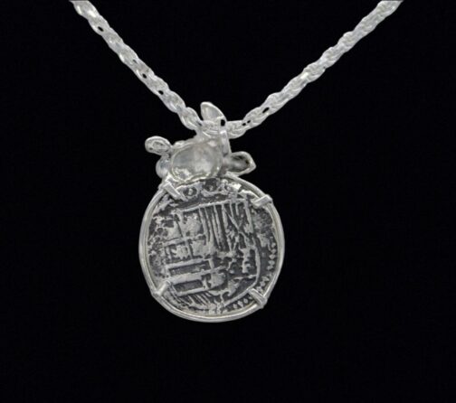 A Silver Medium Turtle Coin pendant from Atocha Shipwreck Coins by The Treasure Shoppe Inc. hangs intricately against a twisted rope chain on a black background.