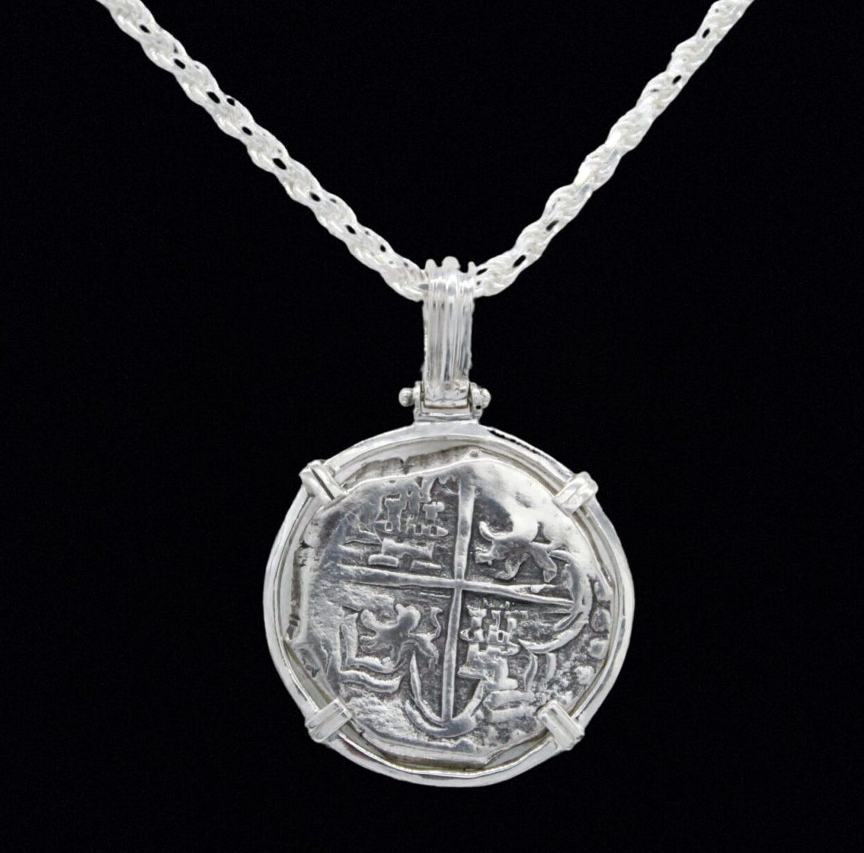 The Treasure Shoppe Inc.s 500 Museum Replica Coin pendant, featuring Atocha Shipwreck design, is set in a four-pronged sterling silver setting. The antique-style piece hangs elegantly from a twisted chain against a black backdrop.