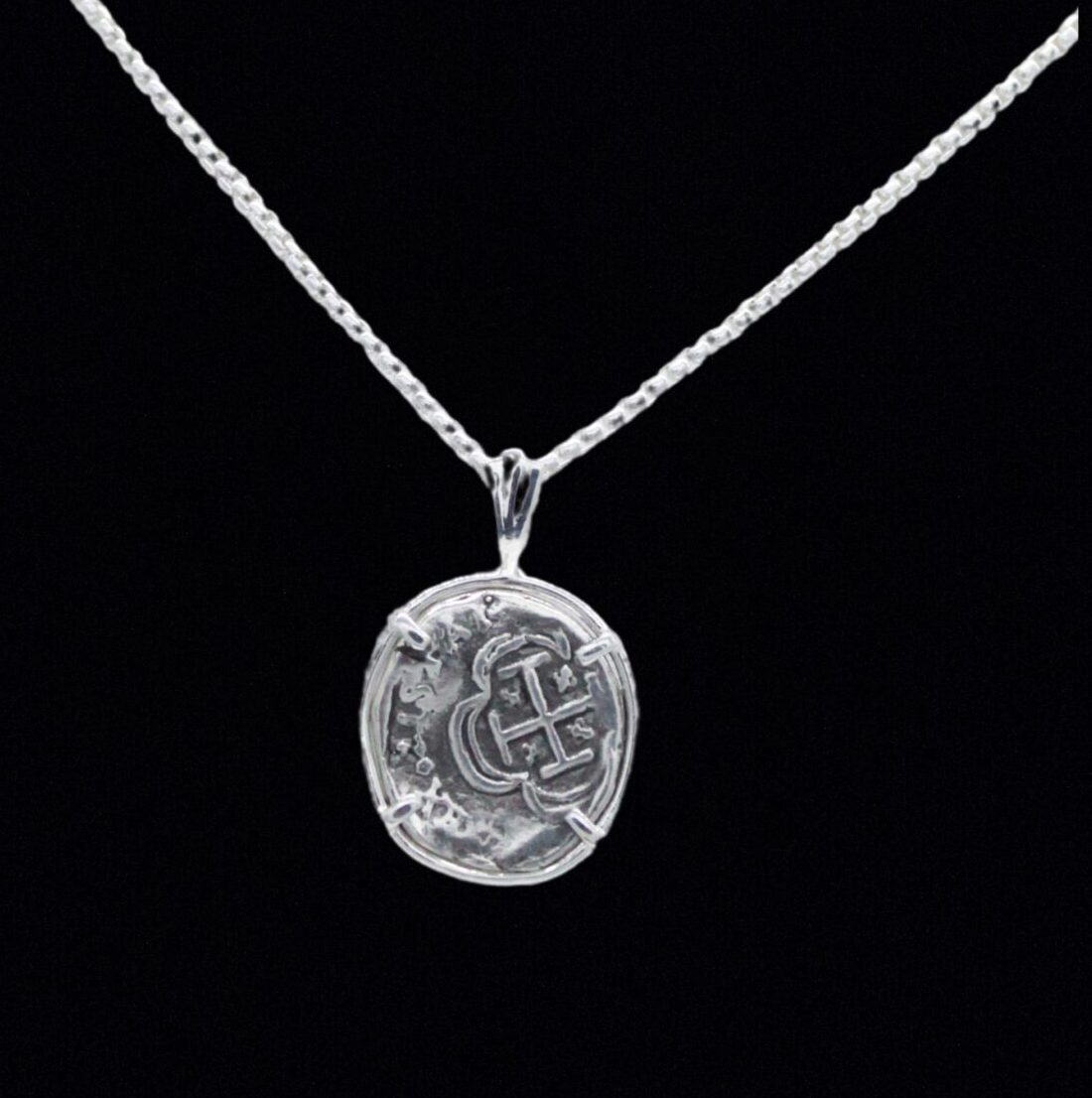 The Treasure Shoppe Inc.s 1 Reale Coin- Atocha Shipwreck Coins pendant showcases intricate oval details on a delicate sterling silver chain, set against a black backdrop, exuding a historic charm akin to cherished Atocha coins.