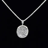 The Treasure Shoppe Inc.s 1 Reale Coin- Atocha Shipwreck Pendant is a historic piece featuring intricate markings on a sterling silver round pendant with a black background, suspended from a thin, textured chain.