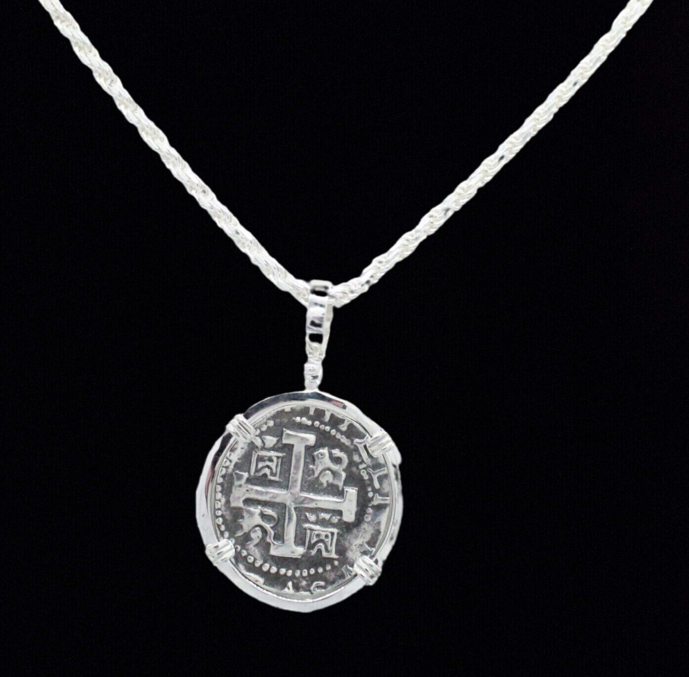 The Treasure Shoppe Inc. presents the 8 Reale Triple Prong Coin Pendant, inspired by Atocha shipwreck coins. This pendant showcases intricate patterns and historic charm, reminiscent of Atocha coins, beautifully dangles from a textured chain against a black background (chain not included).