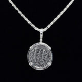 The Treasure Shoppe Inc.s 8 Reale Triple Prong Coin pendant showcases an ornate, engraved circular design with symbols and numbers, evoking historic charm. The sterling silver piece hangs elegantly on a twisted chain against a black background.
