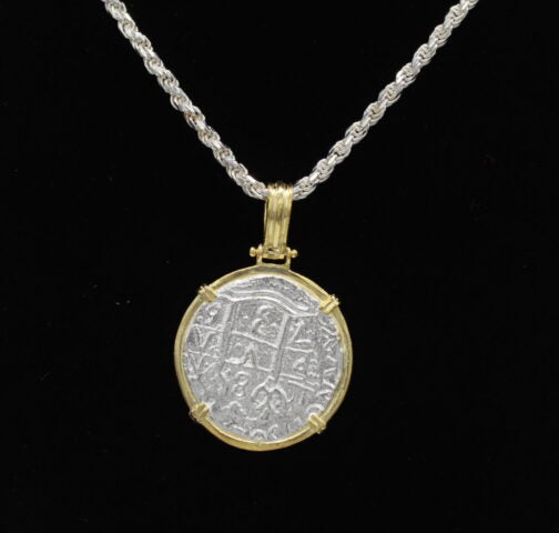 The Treasure Shoppe Inc.s Gold Plated Large Framed Coin features an Atocha Shipwreck coin encased in gold, suspended on a twisted silver chain. This historic coin, with detailed engravings, exudes timeless charm against a black backdrop.