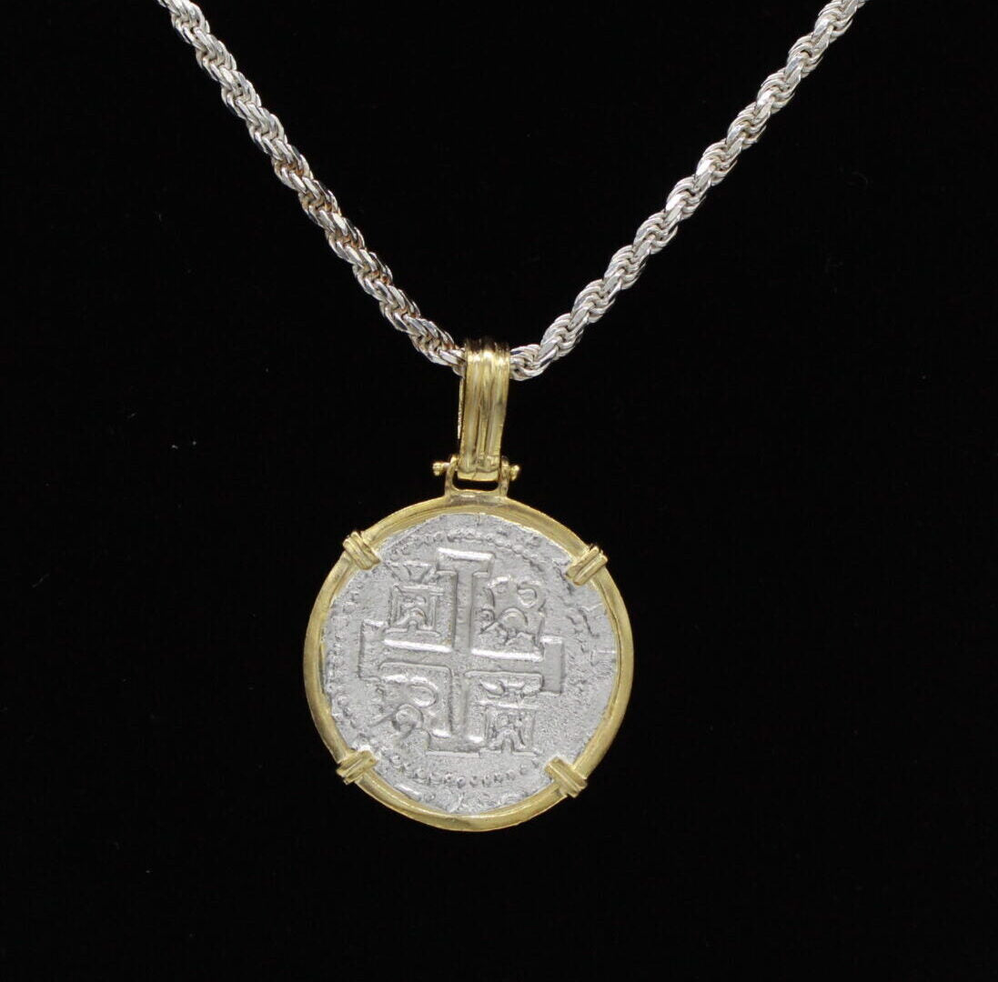 The Treasure Shoppe Inc.s Gold Plated Large Framed Coin Pendant from the Atocha Shipwreck exudes historic charm with its intricate design, elegantly set in a gold bezel. It blends timeless allure with contemporary style when displayed against a black background.