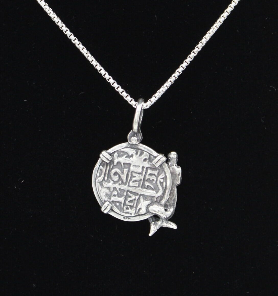 The Treasure Shoppe Inc.s Medium Mermaid Coin from the Atocha Shipwreck Coins collection features a sterling silver bezel with intricate engravings and a mermaid figure. This pendant elegantly hangs on a chain against a black background.