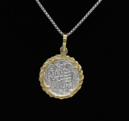 The Treasure Shoppe Inc.s Gold Plated Rope Bezel Coin, inspired by Atocha Shipwreck Coins, features intricate designs on a black background with a gold plated rope bezel.