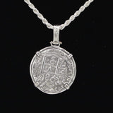 On a black backdrop, a round silver pendant from The Treasure Shoppe Inc.s 8 Reale 2 Prong Coin-Atocha Shipwreck Coins collection hangs in a twisted sterling silver bezel. Resembling Atocha Coins, its secured by four brackets and showcases intricate symbols and patterns for an antique look.