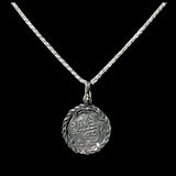The Treasure Shoppe Inc. presents the Silver Rope Bezel Coin pendant, inspired by Atocha shipwreck coins, featuring intricate designs with a gold-plated over silver bezel and an ancient coin pendant, elegantly framed by a twisted silver rope and set against a black background.