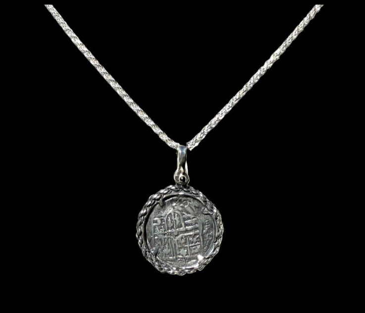 The Treasure Shoppe Inc. presents the Silver Rope Bezel Coin pendant, inspired by Atocha shipwreck coins, featuring intricate designs with a gold-plated over silver bezel and an ancient coin pendant, elegantly framed by a twisted silver rope and set against a black background.